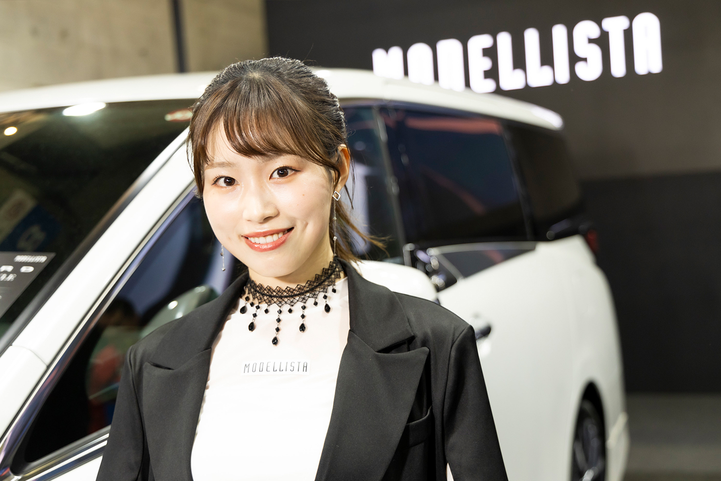 MODELLISTA仕様のアルファードの前で笑顔を見せる美女