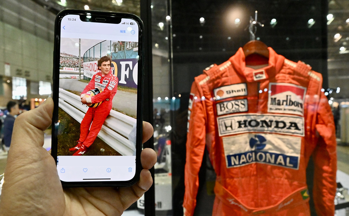 セナ没後30年のコーナーに展示された彼のヘルメットとレーシングスーツ。携帯の画面は筆者が92年のF1日本GPで撮影したリタイヤ直後のセナ。