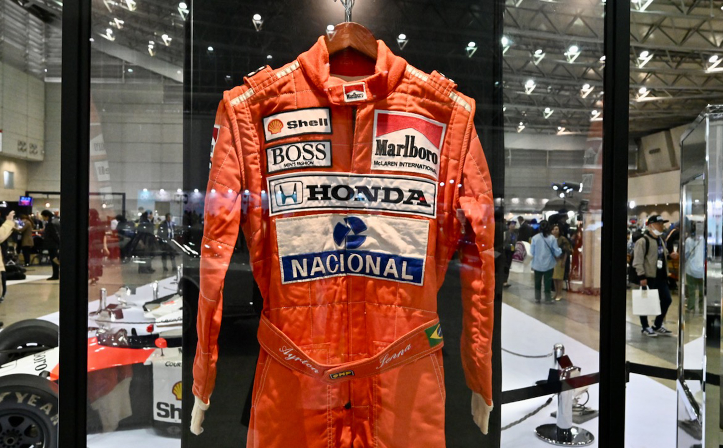 セナ没後30年のコーナーに展示された彼のヘルメットとレーシングスーツ。携帯の画面は筆者が92年のF1日本GPで撮影したリタイヤ直後のセナ。