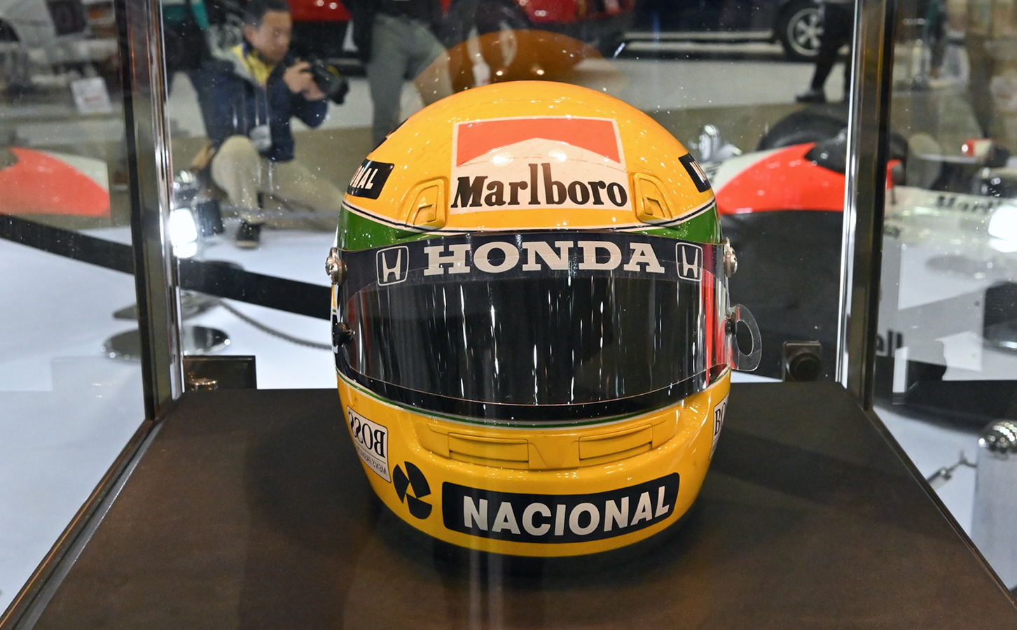セナ没後30年のコーナーに展示された彼のヘルメットとレーシングスーツ。携帯の画面は筆者が92年のF1日本GPで撮影したリタイヤ直後のセナ。